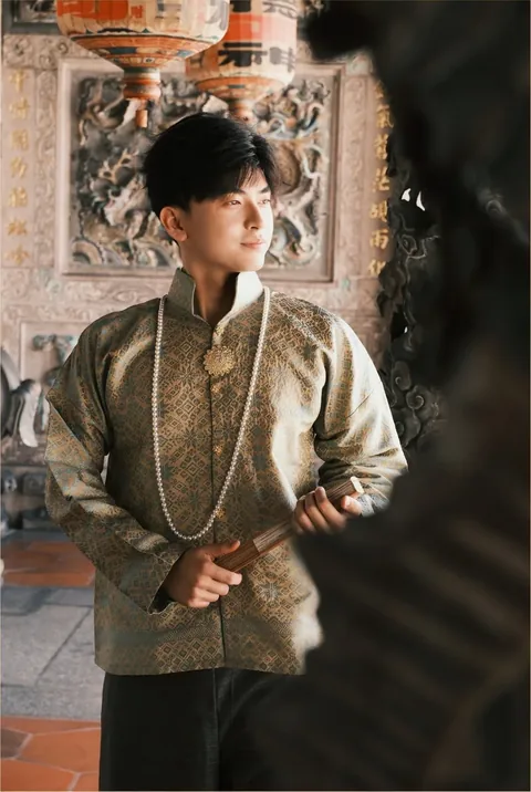 身穿金色织锦外套、手持折扇的男子，背后是庙宇雕花